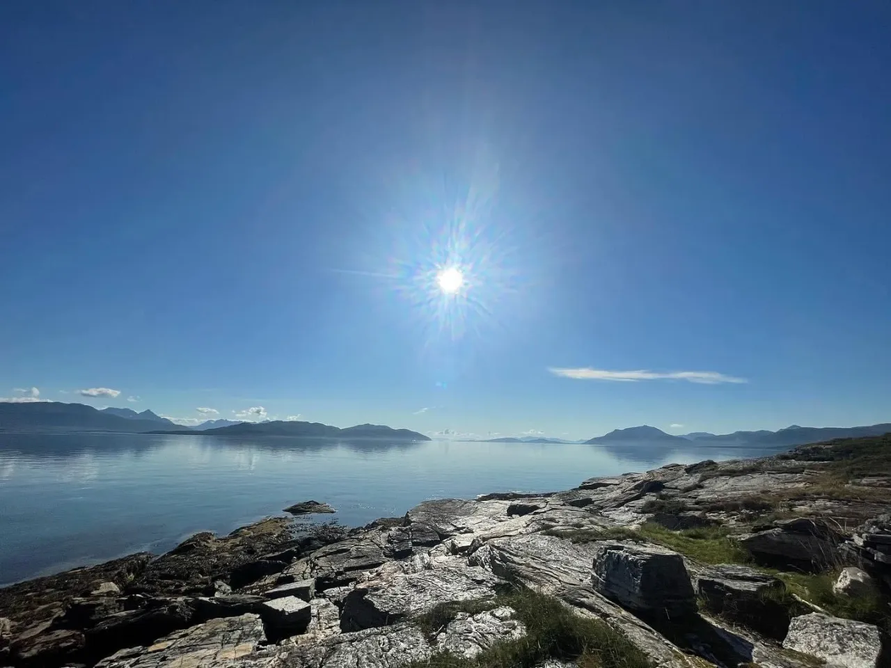 Sun over the fjord seen from smooth coastal rocks