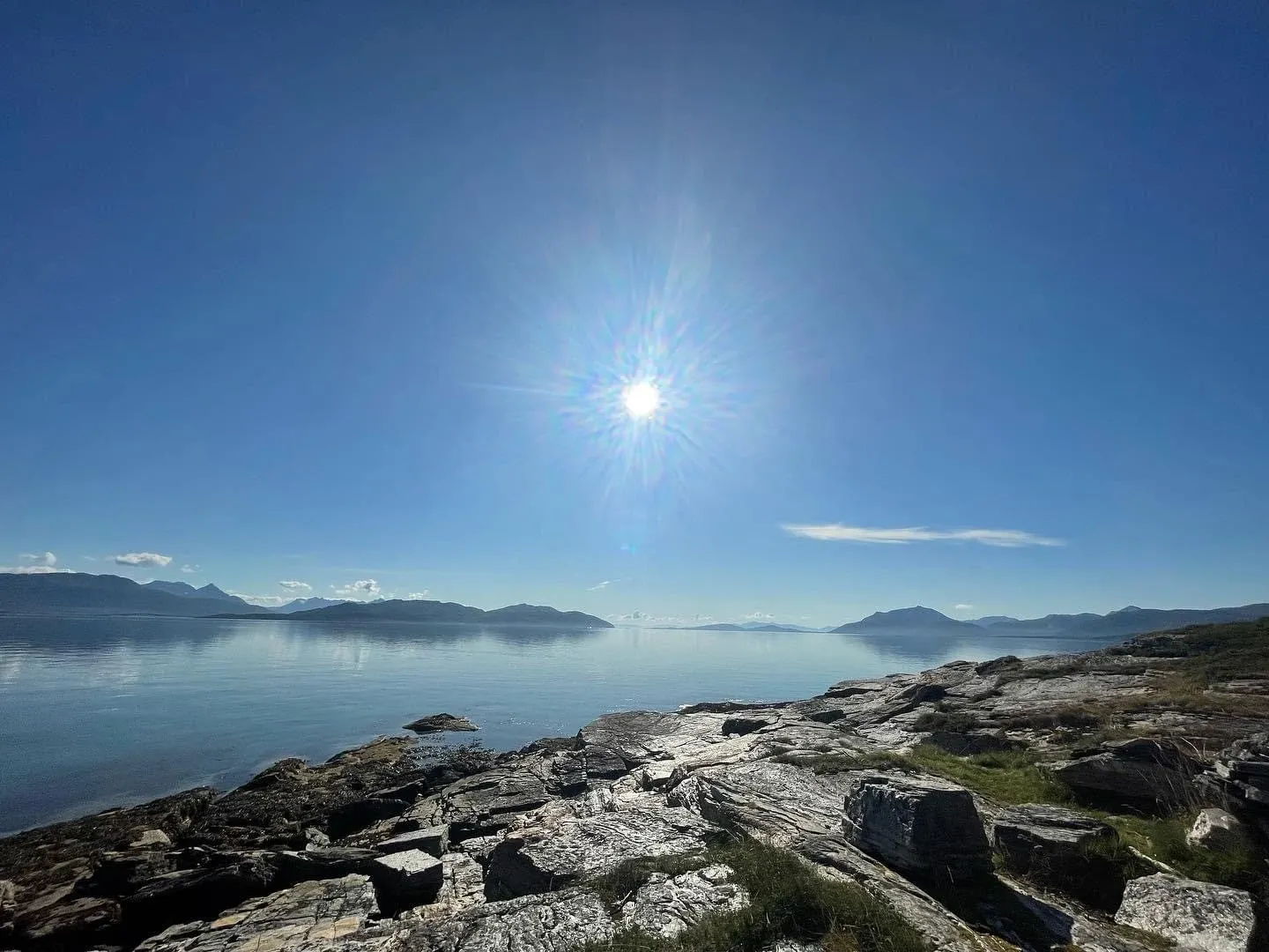 Sun over the fjord seen from smooth coastal rocks on Senja